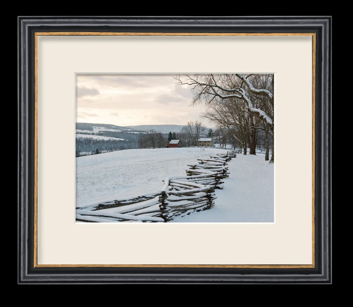 A snowy farm scene matted and framed in a dark wood moulding